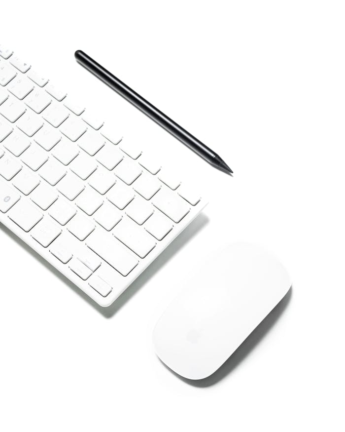 A clean and minimalist workspace featuring a wireless keyboard, mouse, and stylus on a white background.